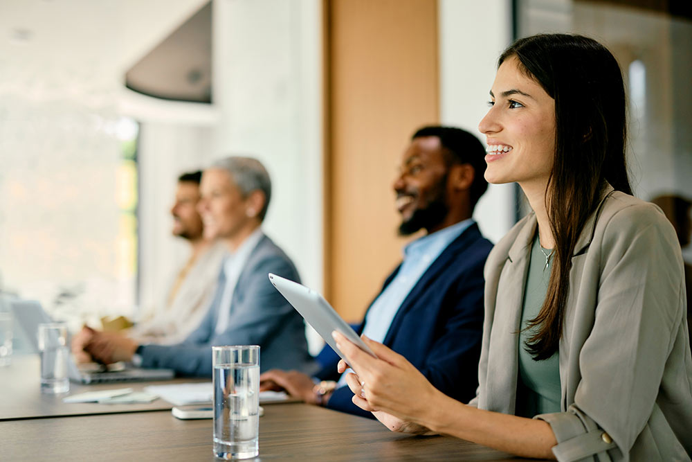 Professionals participating in a business meeting focus on a presentation, collaborating around a conference table with digital devices in a modern office setting